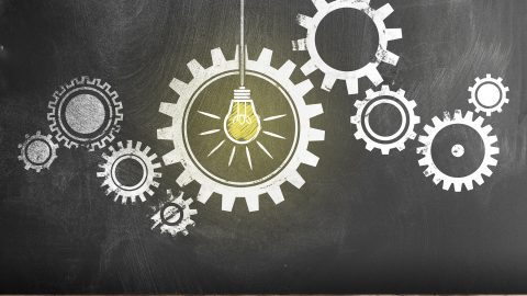 Gear with interlocking Cogwheels with glowing light bulb on blackboard. Stock photo