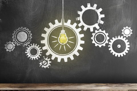 Gear with interlocking Cogwheels with glowing light bulb on blackboard. Stock photo